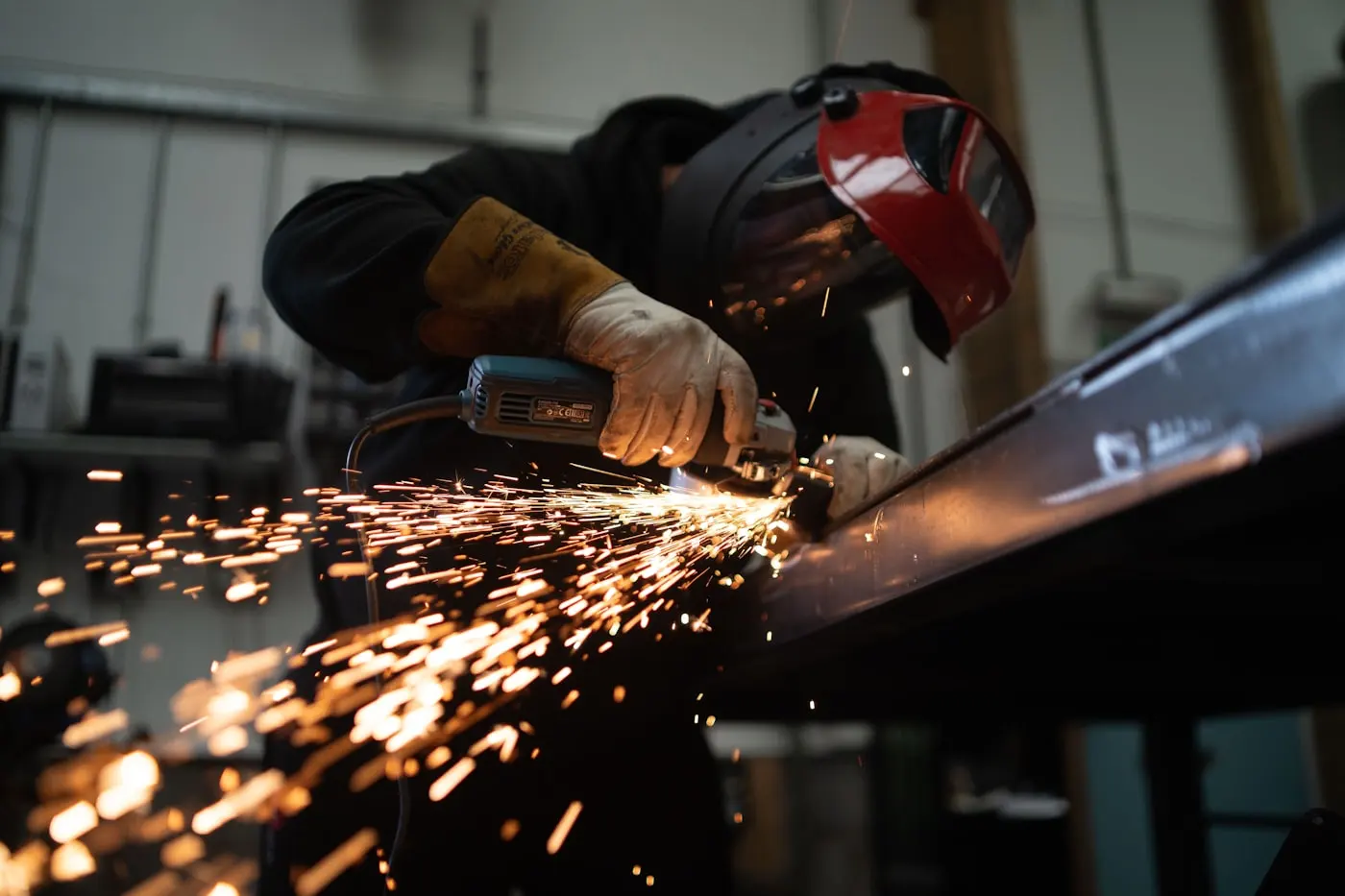 Fabricator in a welding helmet grinding a structural steel beam
